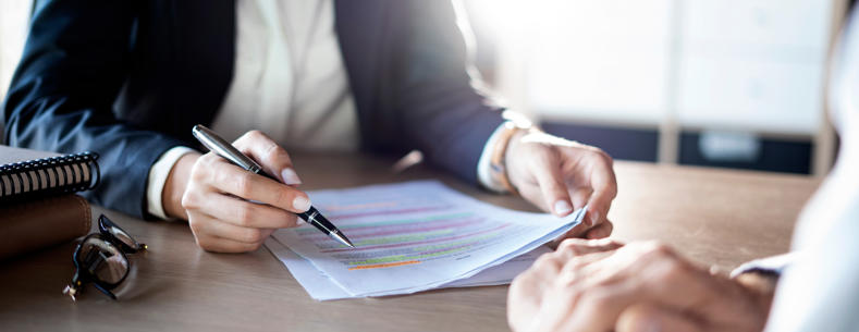 Stock image of two individuals reviewing and discussing a document at a desk in an office setting.