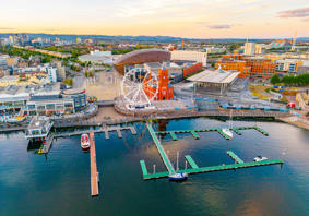 Aerial view of Cardiff Bay showing the waterfront, a Ferris wheel, the red-brick Pierhead Building, and boats moored in the marina