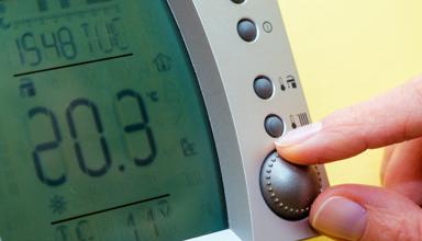 This is a close up image of fingers adjusting a domestic thermostat to a high temperature.