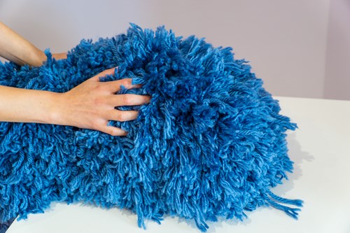 A close up of a person holding a blue fluffy object. The object is made of yarn and is round and long in shape.