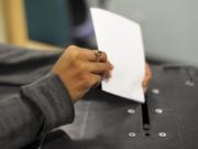 A woman's hand places a ballot paper into a ballot box