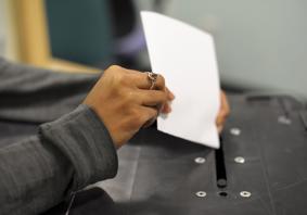 A woman's hand places a ballot paper into a ballot box
