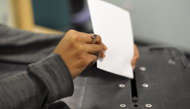 A woman's hand places a ballot paper into a ballot box
