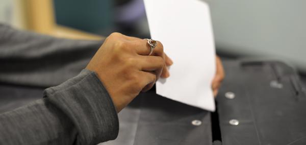 A woman's hand places a ballot paper into a ballot box