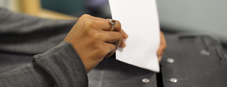 A woman's hand places a ballot paper into a ballot box