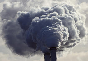 Landscape photograph of industrial chimneys emitting grey smoke. 