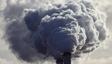 Landscape photograph of industrial chimneys emitting grey smoke. 