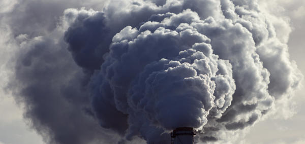Landscape photograph of industrial chimneys emitting grey smoke. 