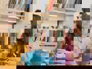 Two women sit at a table with a pot of tea, having a conversation in sign language.