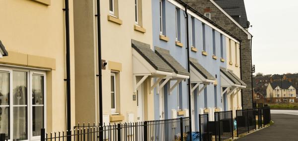 Row of newly built terraced houses with cream and blue walls, small porches, and black railings along the front