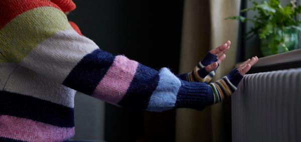 Picture of a woman putting her hands on a radiator for warmth.