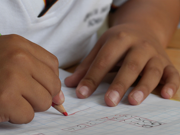 A school pupil writing on a piece of paper with a red pencil.