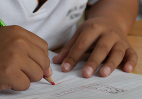 A school pupil writing on a piece of paper with a red pencil.