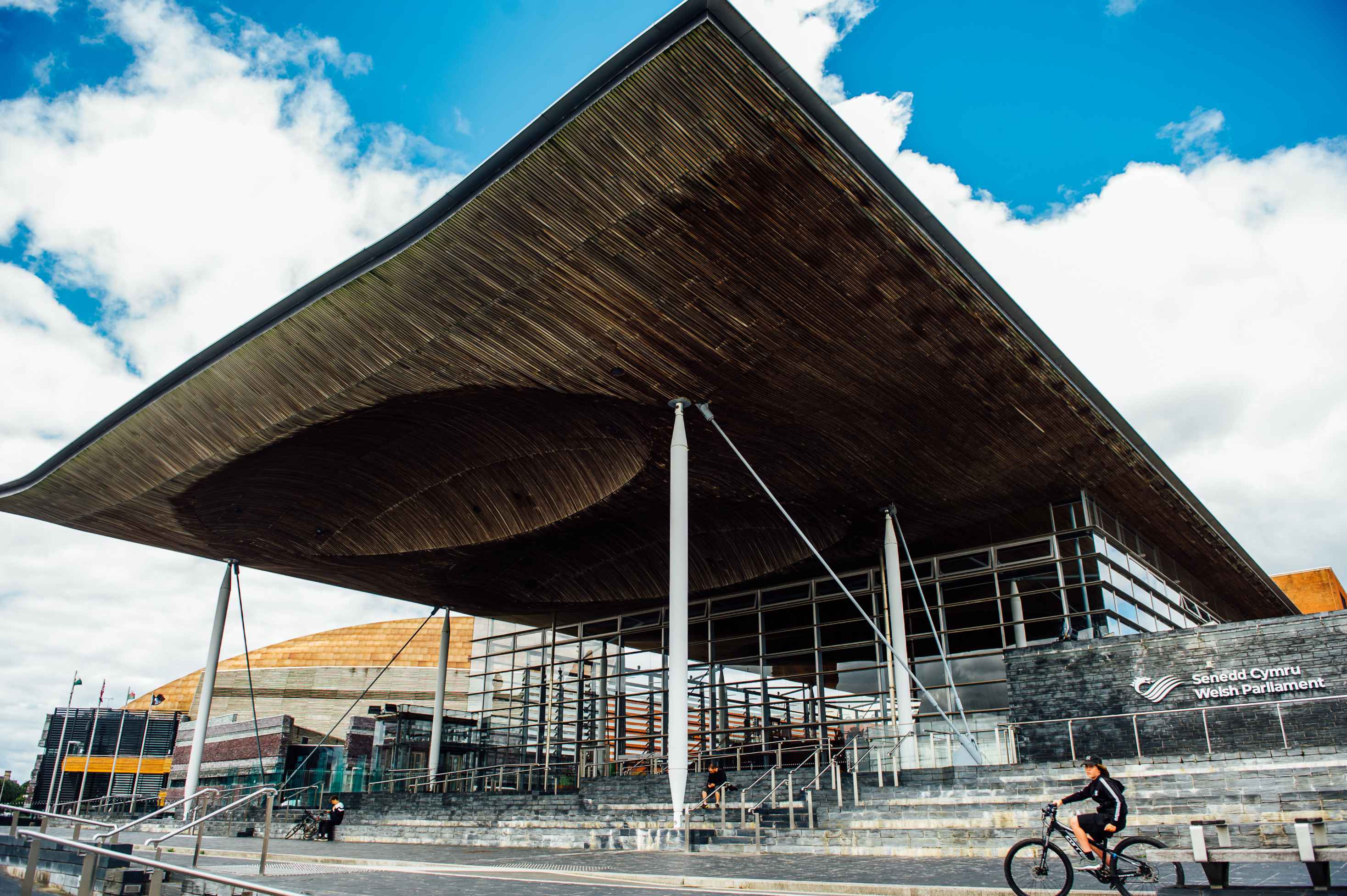 An image of the exterior of the Senedd building in Cardiff Bay, with blue sky and clouds in the background. 