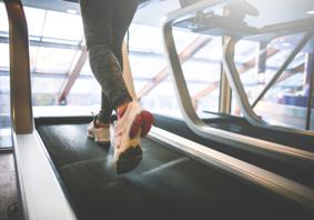 A person’s legs wearing sports trousers and trainers running on a treadmill with windows in the background.