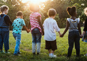 Children playing outdoors on a grassy area, with several children running and interacting in a park-like setting under natural daylight.