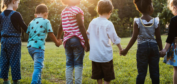 Children playing outdoors on a grassy area, with several children running and interacting in a park-like setting under natural daylight.