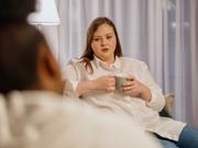 A woman holding a drink sitting opposite another person 