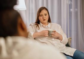 A woman holding a drink sitting opposite another person 