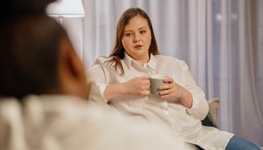 A woman holding a drink sitting opposite another person 