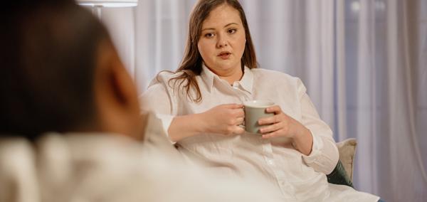 A woman holding a drink sitting opposite another person 