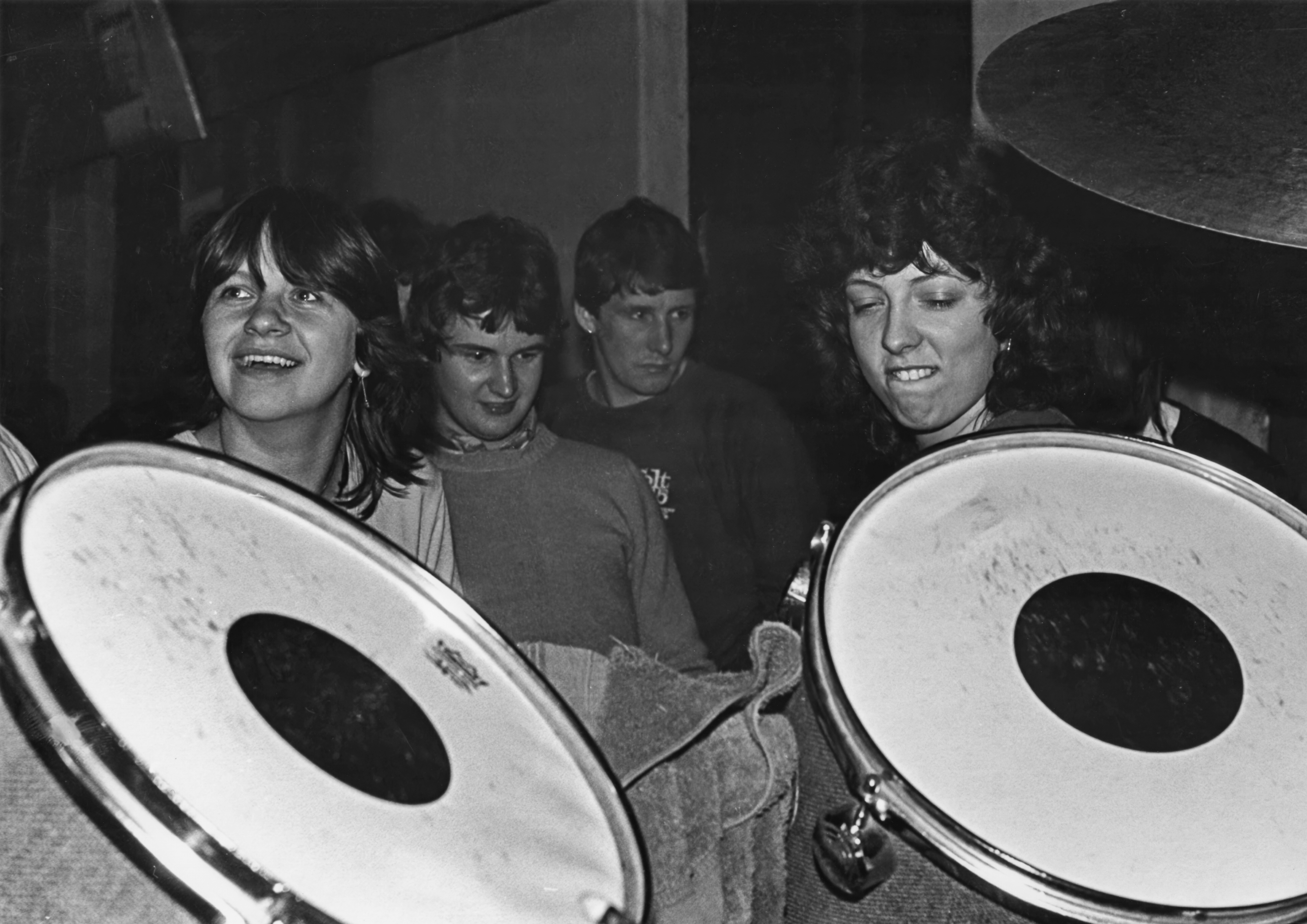 Black-and-white photograph of people gathered around large percussion instruments in a busy music venue.