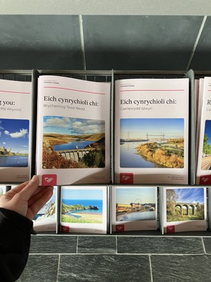 ‘Representing you’ booklets arranged in a metal holder, each showing a Welsh constituency with images and titles; one booklet is held in the foreground.