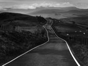 Photo showing large jagged rocks on a shore-front. In the distance the sea is just visible. The grey, moody sky is full of clouds.