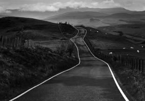 Photo showing large jagged rocks on a shore-front. In the distance the sea is just visible. The grey, moody sky is full of clouds.