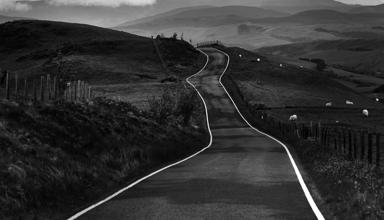 Photo showing large jagged rocks on a shore-front. In the distance the sea is just visible. The grey, moody sky is full of clouds.