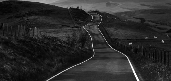 Photo showing large jagged rocks on a shore-front. In the distance the sea is just visible. The grey, moody sky is full of clouds.