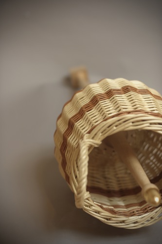 Woven wicker mace with a cylindrical, basket-like head and a protruding wooden handle, combining the form of a domestic basket with a mace silhouette.