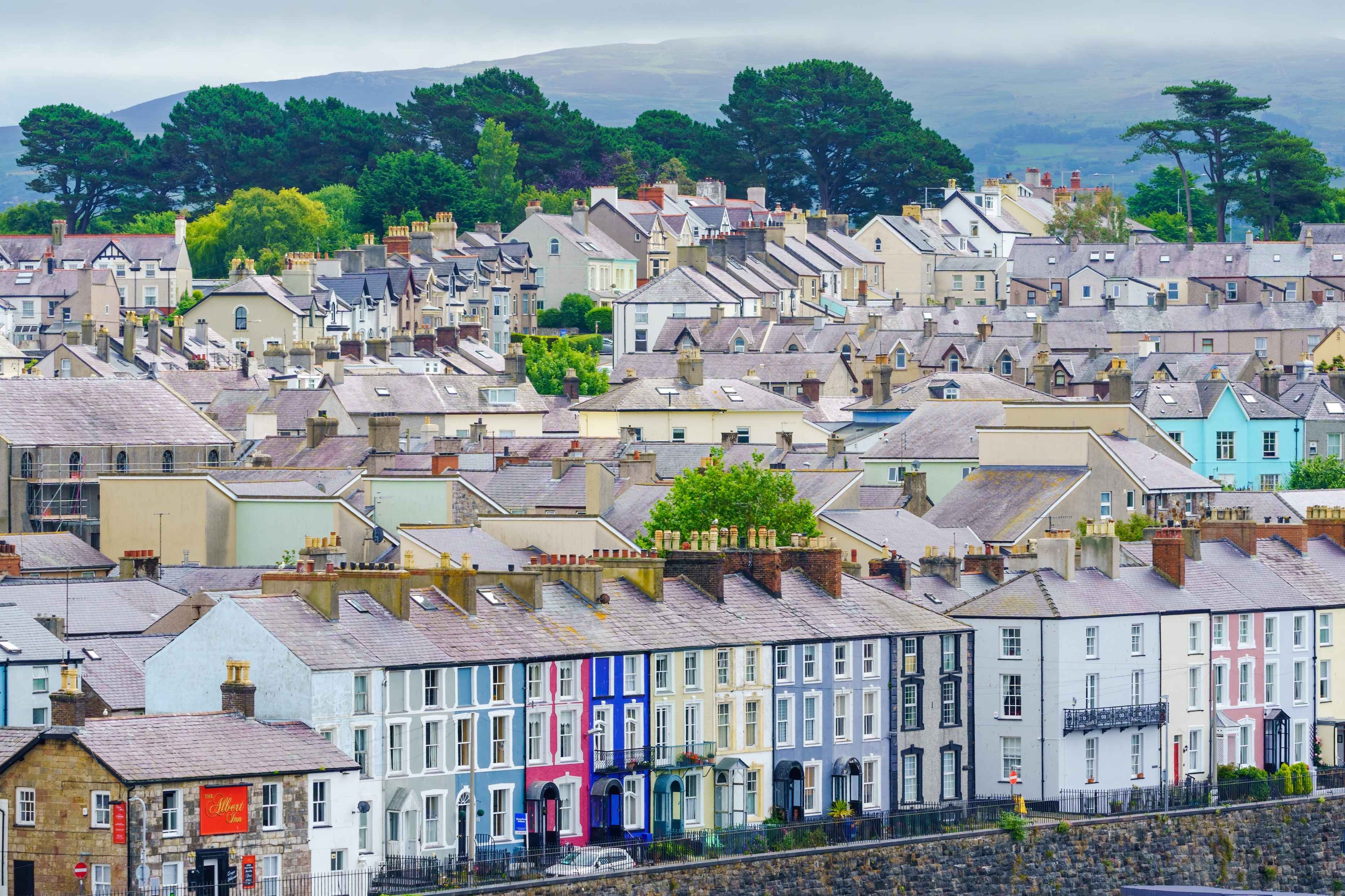 An image of homes and rooflines in a Welsh town or village. The most prominent houses in the image have colourful and striking frontages and a local pub on the corner. 