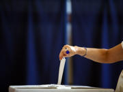 Female arm placing a ballot paper in a ballot box with a blue background.