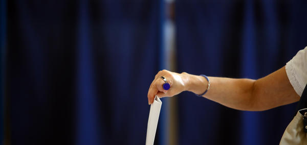 Female arm placing a ballot paper in a ballot box with a blue background.