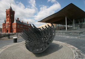 An image of the Senedd and Pierhead buildings, with a sculpture in the foreground. 