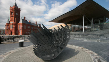 An image of the Senedd and Pierhead buildings, with a sculpture in the foreground. 