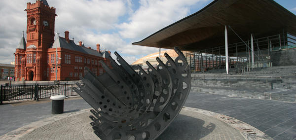 An image of the Senedd and Pierhead buildings, with a sculpture in the foreground. 