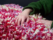 A close up of a person holding a fluffy object. Different colours of yarn have been used including pink, green, red and blue.