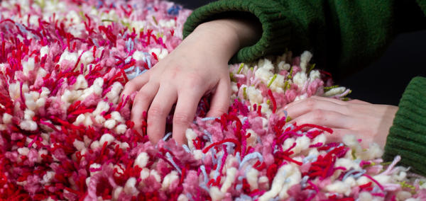 A close up of a person holding a fluffy object. Different colours of yarn have been used including pink, green, red and blue.
