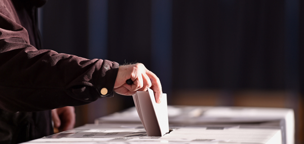 A person putting their folded voting paper into a ballot box.