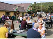 A photo showing people sitting outside Snowdon Mountain Railway Station. The area is busy with people sitting at several picnic tables and talking.