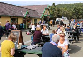 A photo showing people sitting outside Snowdon Mountain Railway Station. The area is busy with people sitting at several picnic tables and talking.