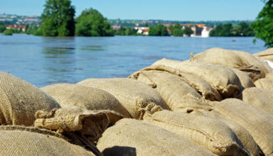A photograph of sandbags in front of a flooded river.