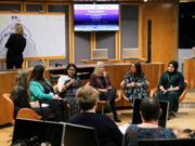 Six women sitting in the center of the Chamber in the Welsh Parliament, taking part in a conference and speaking to microphones.