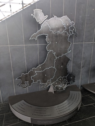 A steel map of Wales showing the boundaries of the Senedd constituencies. Each constituency is numbered and labelled on the base of the display.