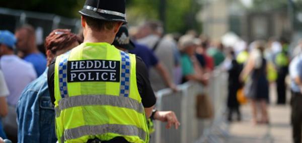 A uniformed police officer wearing a high-visibility yellow vest, standing outdoors, symbolising frontline policing and public visibility.